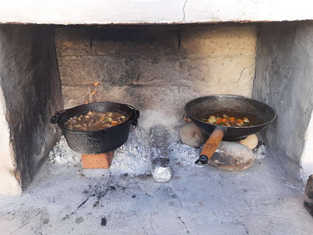 A fire in the braai area, with food cooking in two cast iron pans.