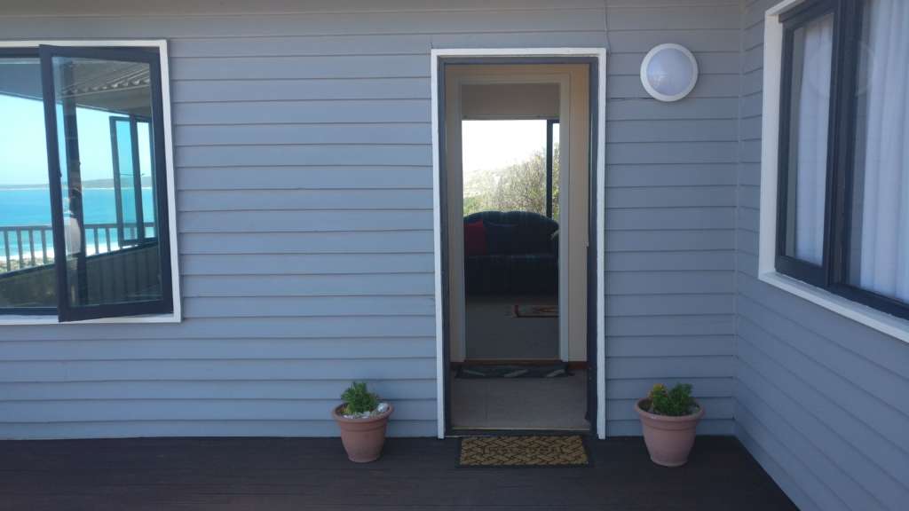 Front door entrance from the deck to the main house at Fonteintjies. Pot plants stand at either side of the door, and there is a welcome mat.