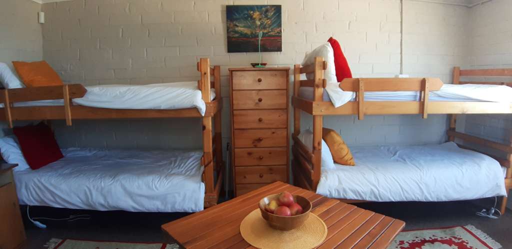 The Annex room at Fonteintjies. On the wall at the centre rear is a chest of drawers, with an abstract oil painting of a sunset above it. Against the wall to the left are two bunk beds, with another two to the right. In the foreground is a square table with a bowl of fruit.