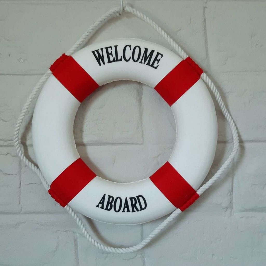 A decorative replica of a ship's life buoy, with the words "Welcome Aboard", hanging on a grey wall in the Annex room at Fonteintjies.