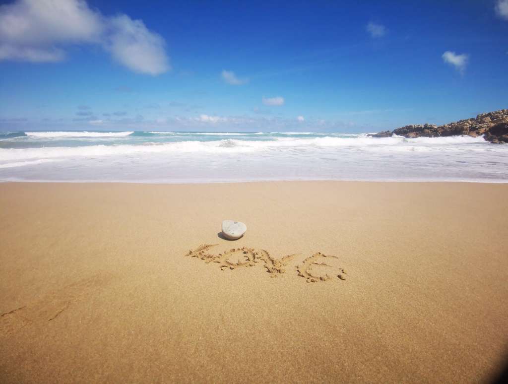 The word LOVE written in the sand on a beach, with the ocean in the backgrond.