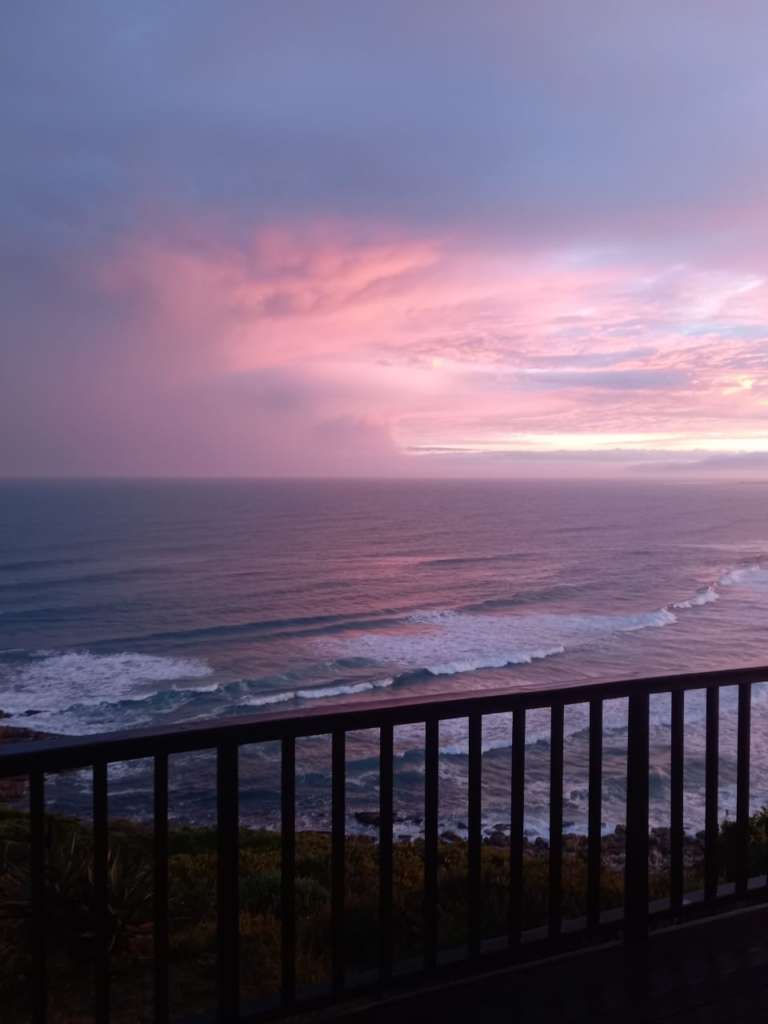 A view of the sea from the deck at Fonteintjies. The sky is many shades of purple as it's sunset. The railing of the deck is in the foreground.