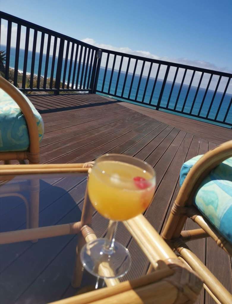A mimosa drink on a small table on the deck. Two comfortable chairs have a view of the ocean.
